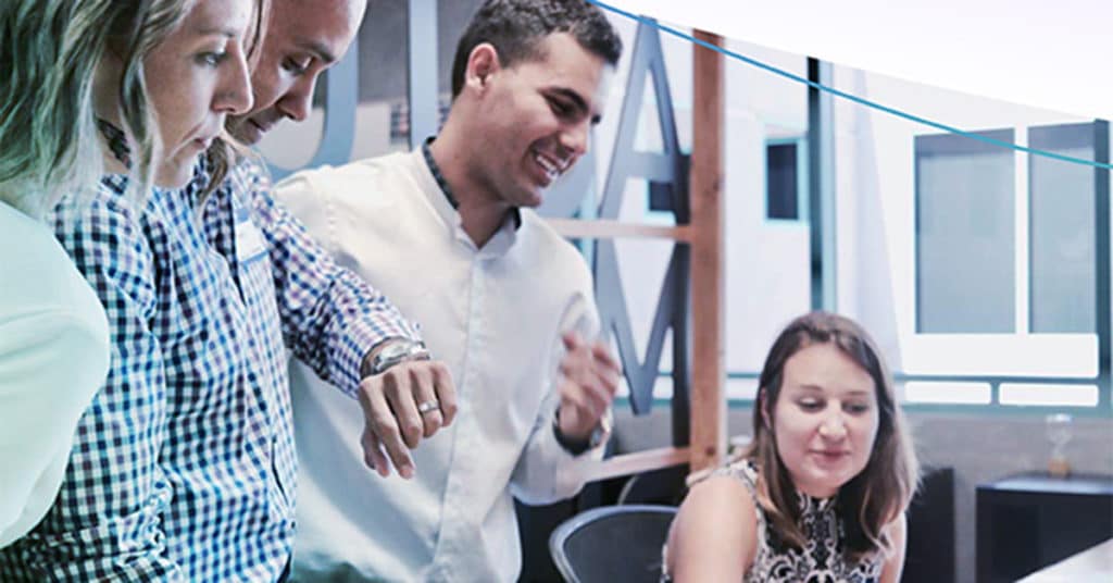 multiple people looking down at computer screen on desk